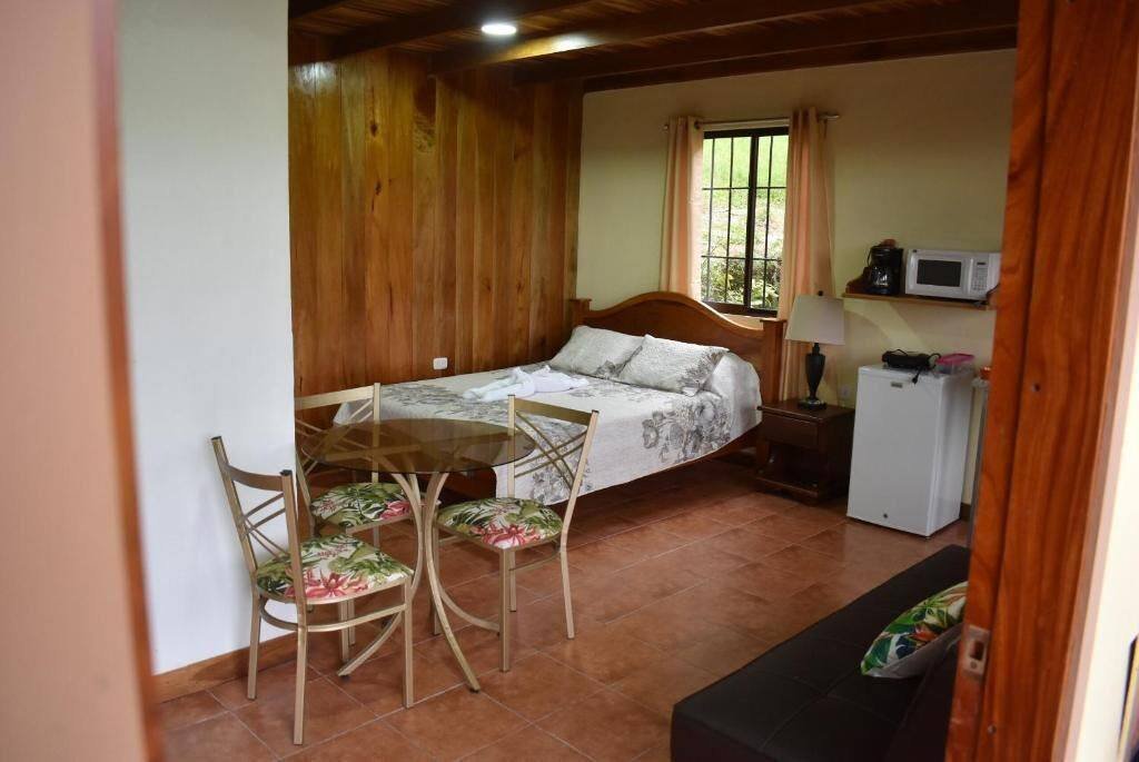 Bed, small table with chairs, microwave and a window with curtains